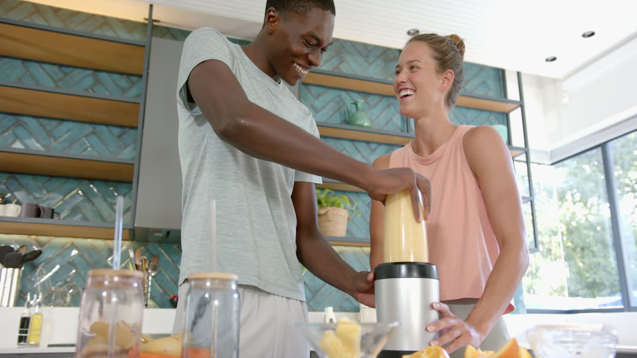 Diverse couple making smoothie in kitchen, at home