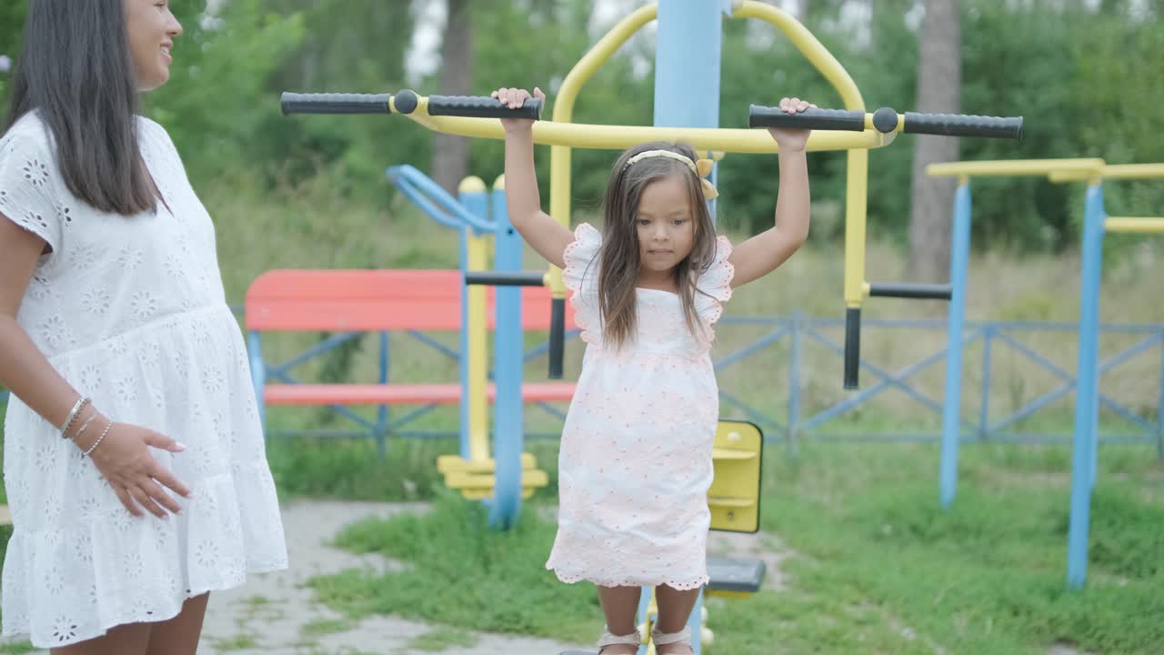 una madre embarazada y su hija joven disfrutan de un tiempo de juego juntos en un patio de recreo en el parque, rodeados de árboles y vegetación