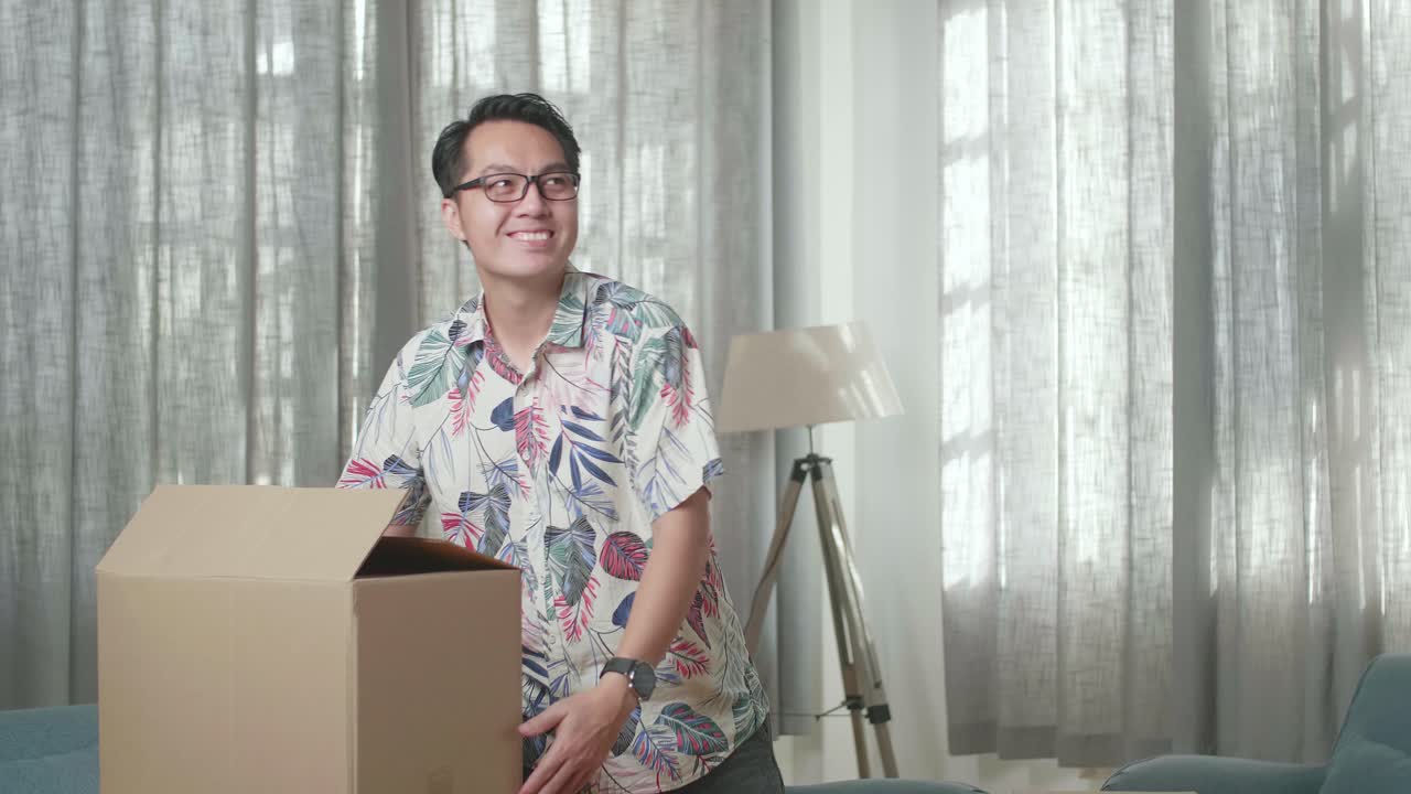 hombre asiático feliz celebrando terminar de llevar una caja de cartón con cosas a una casa nueva. él celebra el día de la mudanza