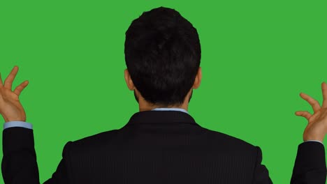 young asian businessman in front of a green screen. talking, turning around and smiling. symbolizing growth, finance, bank, banker, success