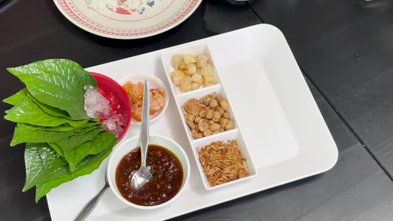 Hands organize Miang Kham savoury leaf wrap ingredients on a white tray under bright, even lighting, with a top-down camera angle and minimal movement