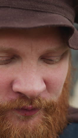 red-bearded man in medieval clothes drinks potion from lid. satisfied village squire uses magical elixir to sustain strength closeup against log house