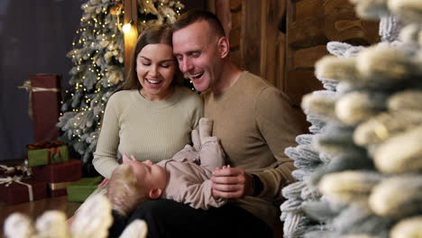 happy loving parents sit close next to each other with their cute little baby on laps. caucasian family celebrating christmas holidays.