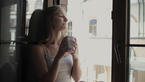 young woman relaxing by the window with a drink