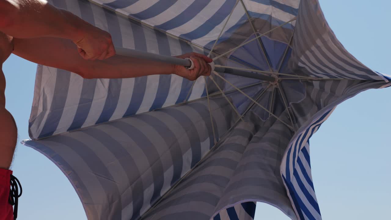 Man Adjusting a Beach Umbrella in Windy Conditions
