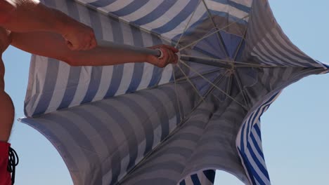 man adjusting a beach umbrella in windy conditions