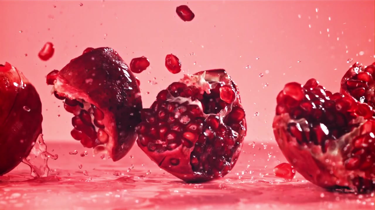 Slow Motion Pomegranate Pieces Falling and Splashing on Pink Surface