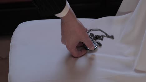 close up of a man picking up a pocket watch off of a chair in preparation as he gets ready for his wedding day