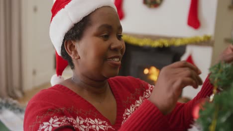 Happy-senior-african-american-woman-decorating-christmas-tree-in-the-living-room