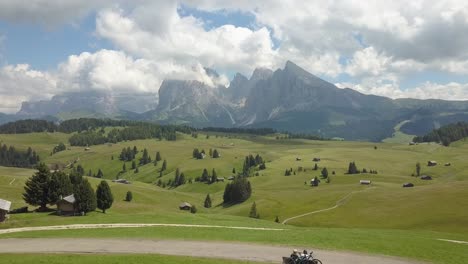 backwards aerial of perfect green hills on a sunny day with large mountains in the background, val gardena, alpe di siussi, dolomites