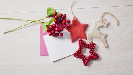 video of christmas decorations, red berries with white and pink cards on wooden background