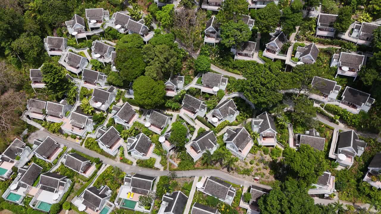 드론 영상은 태국 푸켓에 있는 빌라와 수영장을 가진 울창하고 열대적인 리조트를 포착합니다. 활기찬 초록색과 현대적인 건축물을 보여줍니다.