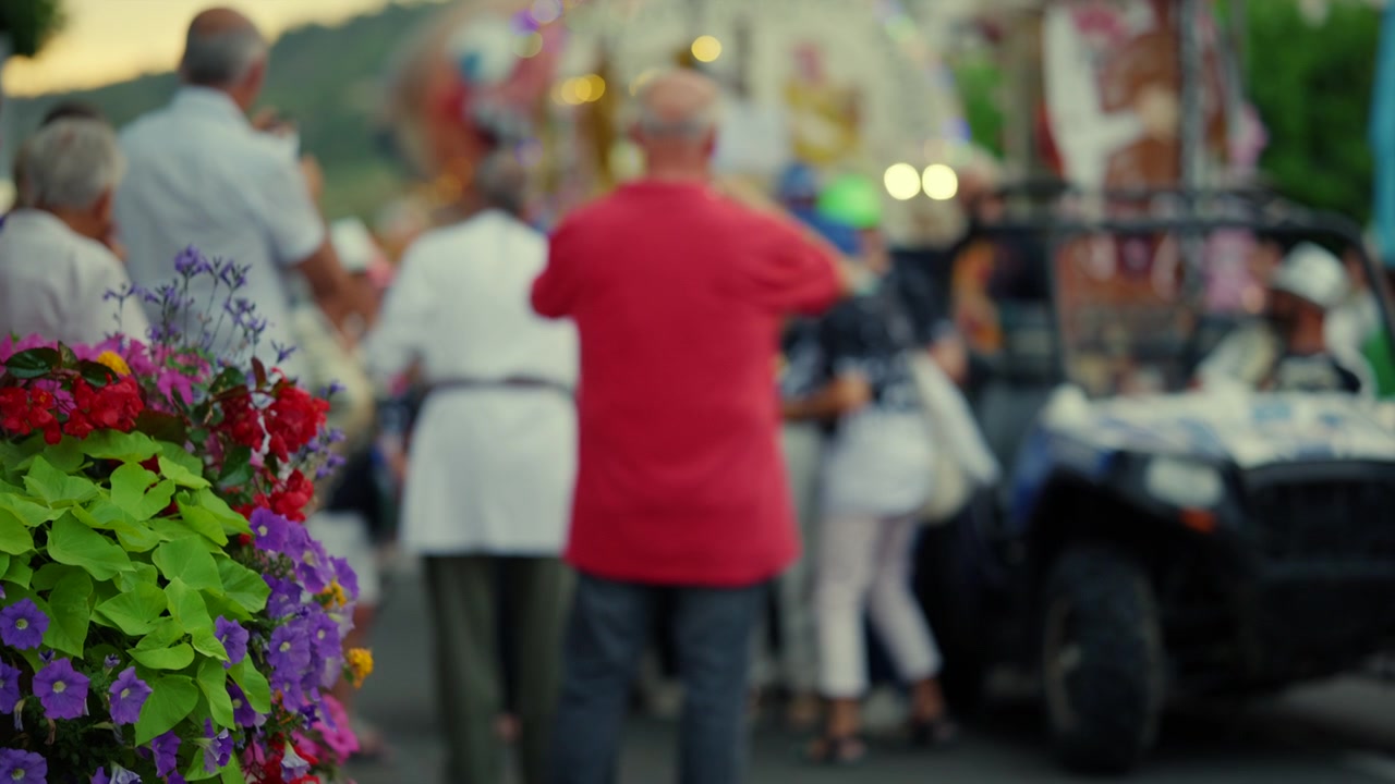 Persone che si godono una vivace festa di strada con fiori colorati in primo piano, creando un'atmosfera estiva vibrante.