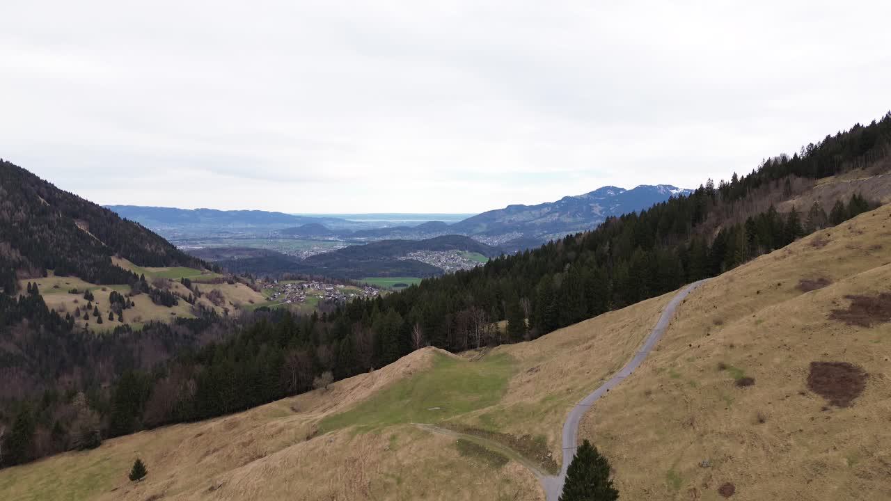 tomada aérea de un avión no tripulado de una carretera de montaña con una amplia vista sobre la ciudad en vorarlberg, austria