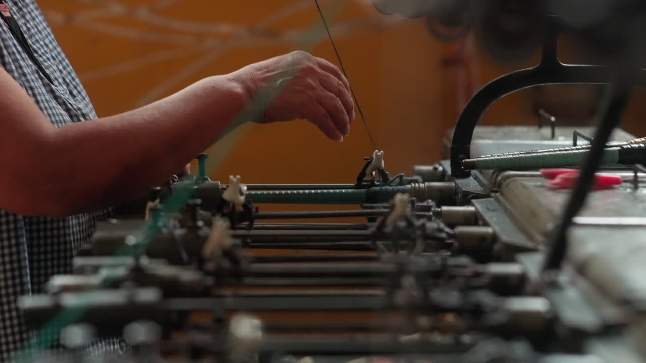 Side view of a woman's arm visible as a professional tapestry weaver works on an antique loom