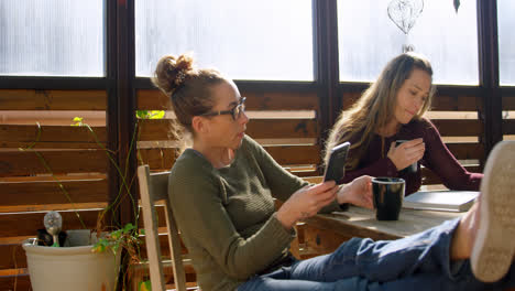 una pareja de lesbianas usando el teléfono móvil y leyendo un libro mientras beben café 4k
