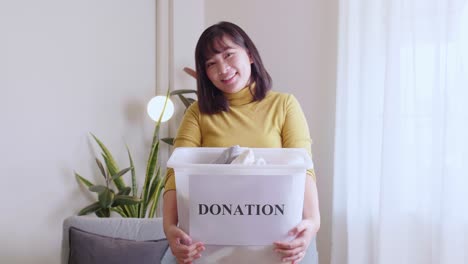 portrait of young asian woman looking at camera holding box with clothes for donation