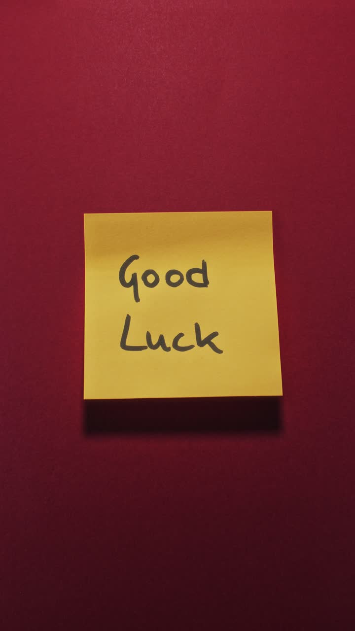 Good Luck message on yellow sticky note against red wall, conveying encouragement and positive wishes
