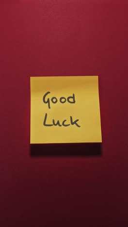 good luck message on yellow sticky note against red wall, conveying encouragement and positive wishes