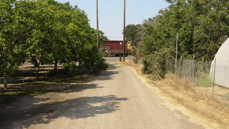 pov shot over a narrow gravel pathway with the view of white greenhouse building on right side and a goods train passing by in the front on a sunny day