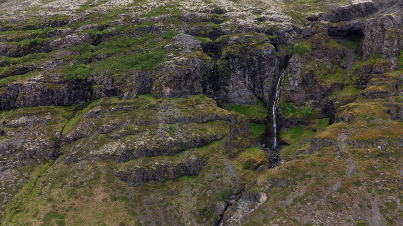 Aerial view of steep mountain cliffs in Sveitarfélagið Hornafjörður, showing layered rock formations, glacial valley textures, and sweeping rugged terrain under an overcast sky