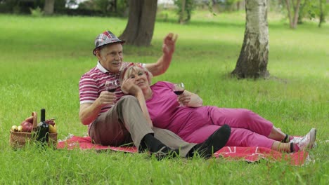 Family-weekend-picnic-in-park.-Active-senior-old-caucasian-couple-sit-on-blanket-and-drink-wine