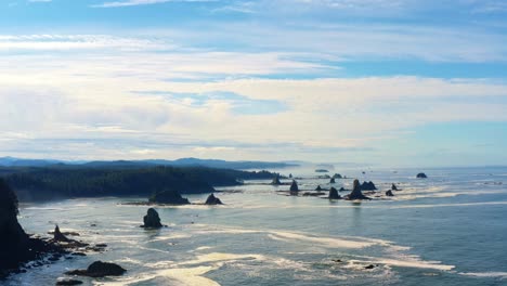 stunning dolly out aerial drone shot of the gorgeous third beach in forks, washington with large rock formations, cliffs, small waves and sea foam on a warm sunny summer morning