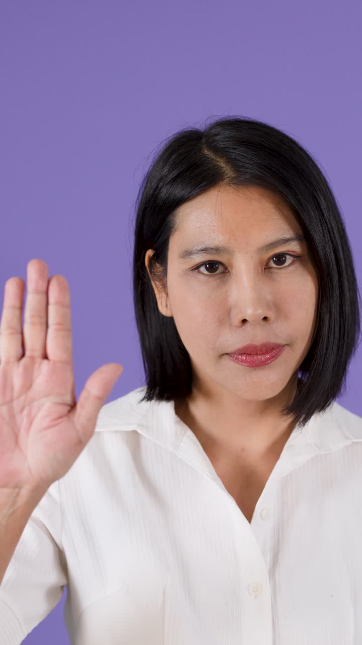 A woman with short black hair makes a firm stop gesture against a purple background