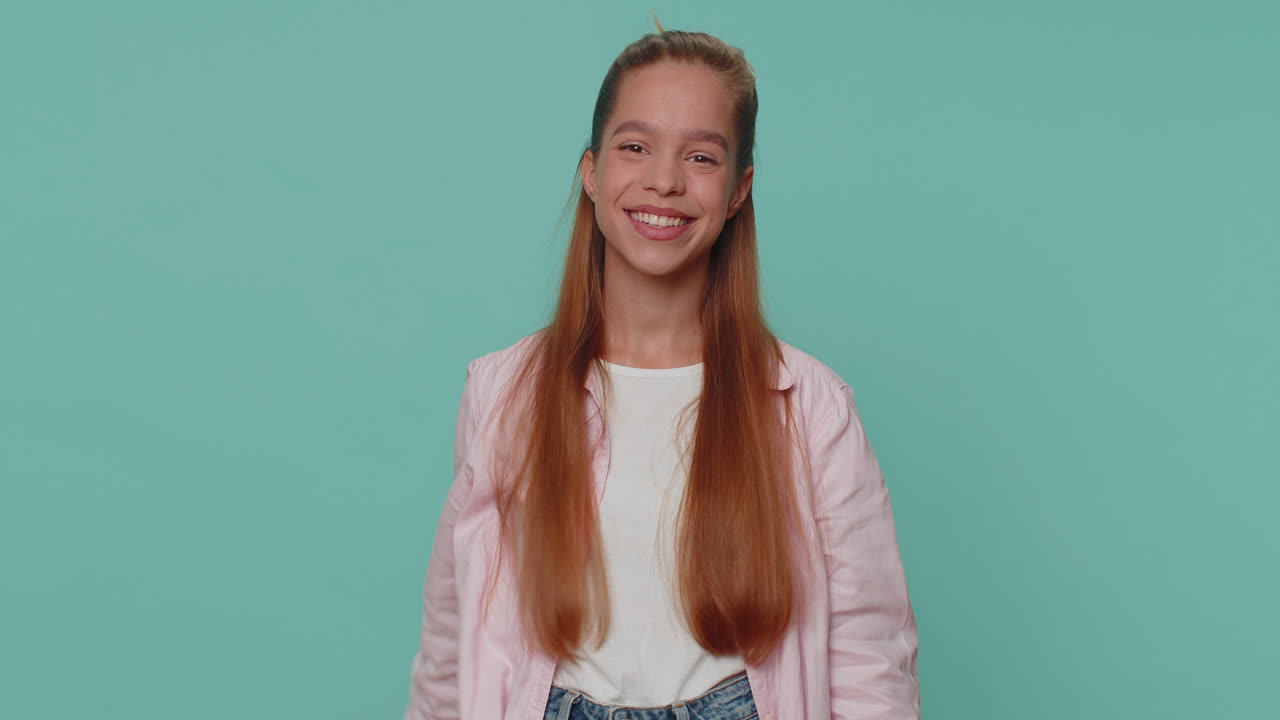 Menina adorável surge por baixo acenando com a palma da mão, cumprimentando com um sorriso amigável e acolhedor.