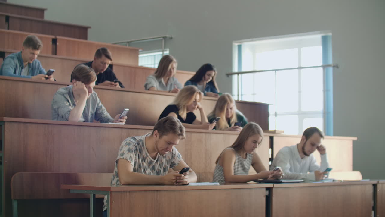 un gran grupo de hombres y mujeres se sientan en el auditorio de la universidad y ven videos en internet en teléfonos inteligentes escriben mensajes y chatan en línea. comportamiento antisocial de los introvertidos. el problema moderno de la sociedad