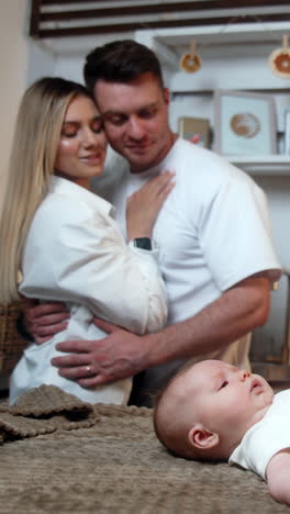 mother and father with their newborn son in the kitchen. happy parents embrace looking at their baby. vertical video