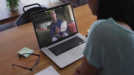 Mixed-race-businesswoman-sitting-at-desk-using-laptop-having-video-call-with-male-colleague