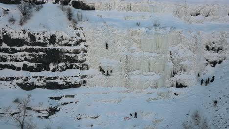 Toma-Aérea-De-Retroceso-Que-Muestra-A-Un-Escalador-De-Hielo-En-Una-Empinada-Pared-De-Montaña-Nevada-En-El-Cañón-De-Provo,-Utah