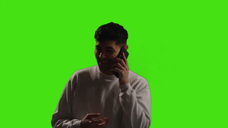 Young-Man-Making-A-Call-On-Mobile-Phone-Standing-Against-Green-Screen-Studio-Background-With-Low-Key-Lighting-2