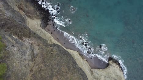 secluded beach sea ocean waves over rocky coastline, aerial drone top-down view