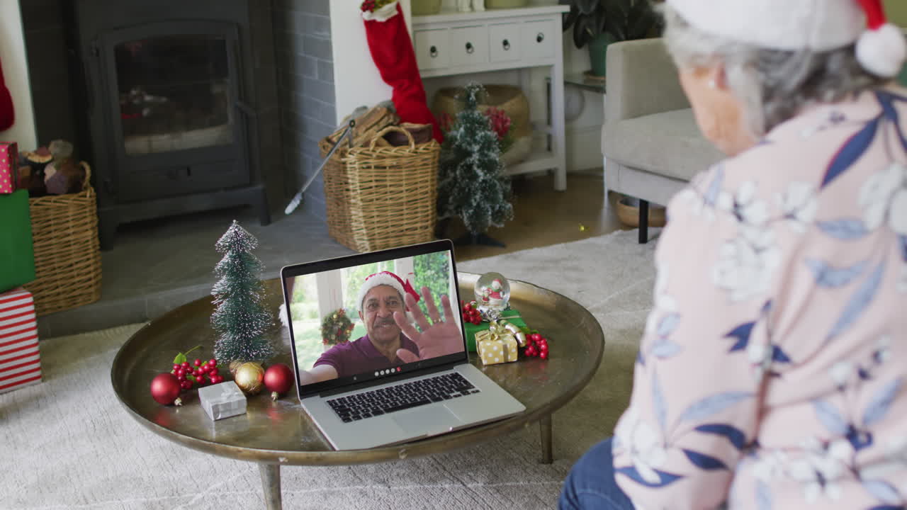 mujer mayor caucásica con sombrero de santa usando una computadora portátil para una videollamada de navidad con un hombre en la pantalla