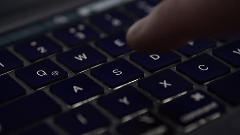 a close-up view of a person's finger pressing the s key on a dark-colored laptop keyboard. the image captures the glossy keys and sleek design, emphasizing the tactile interaction with the device