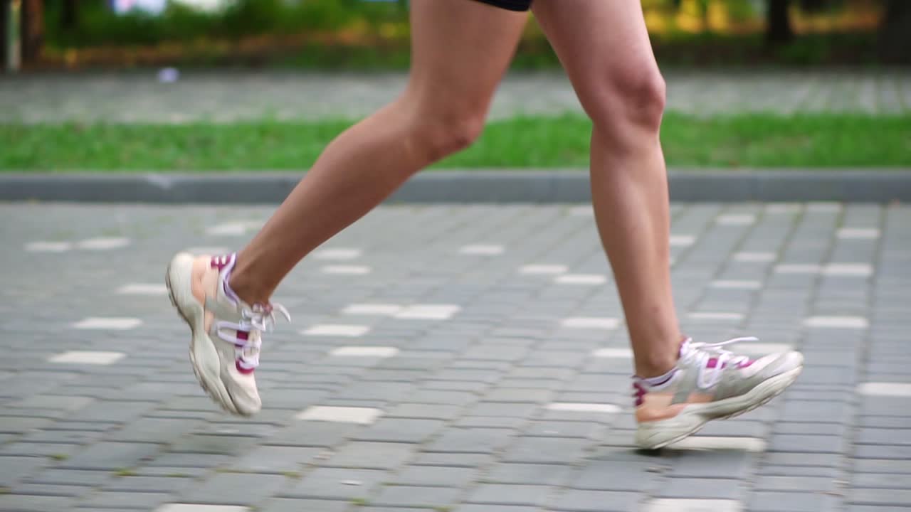Female athlete's feet running at the park. Fitness woman jogging outdoors. Exercising on park pavement. Healthy, fitness