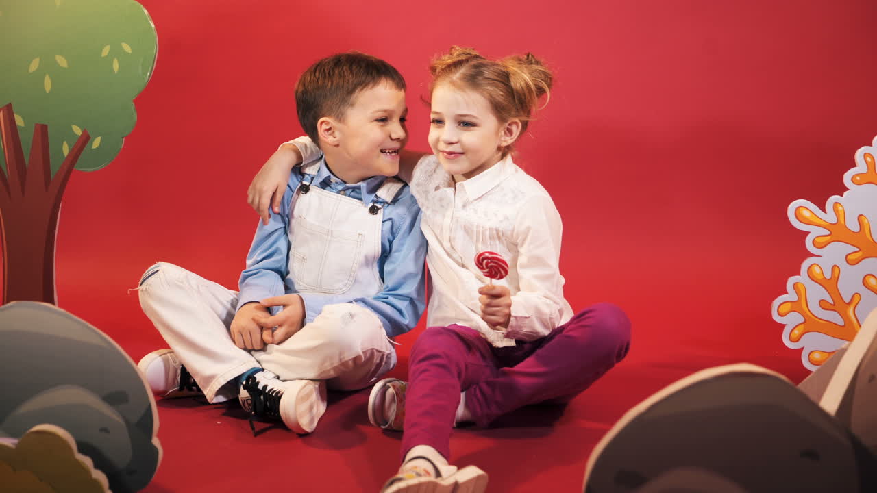 Two children. Boy and a girl with large Lollipop. Studio portrait on red background