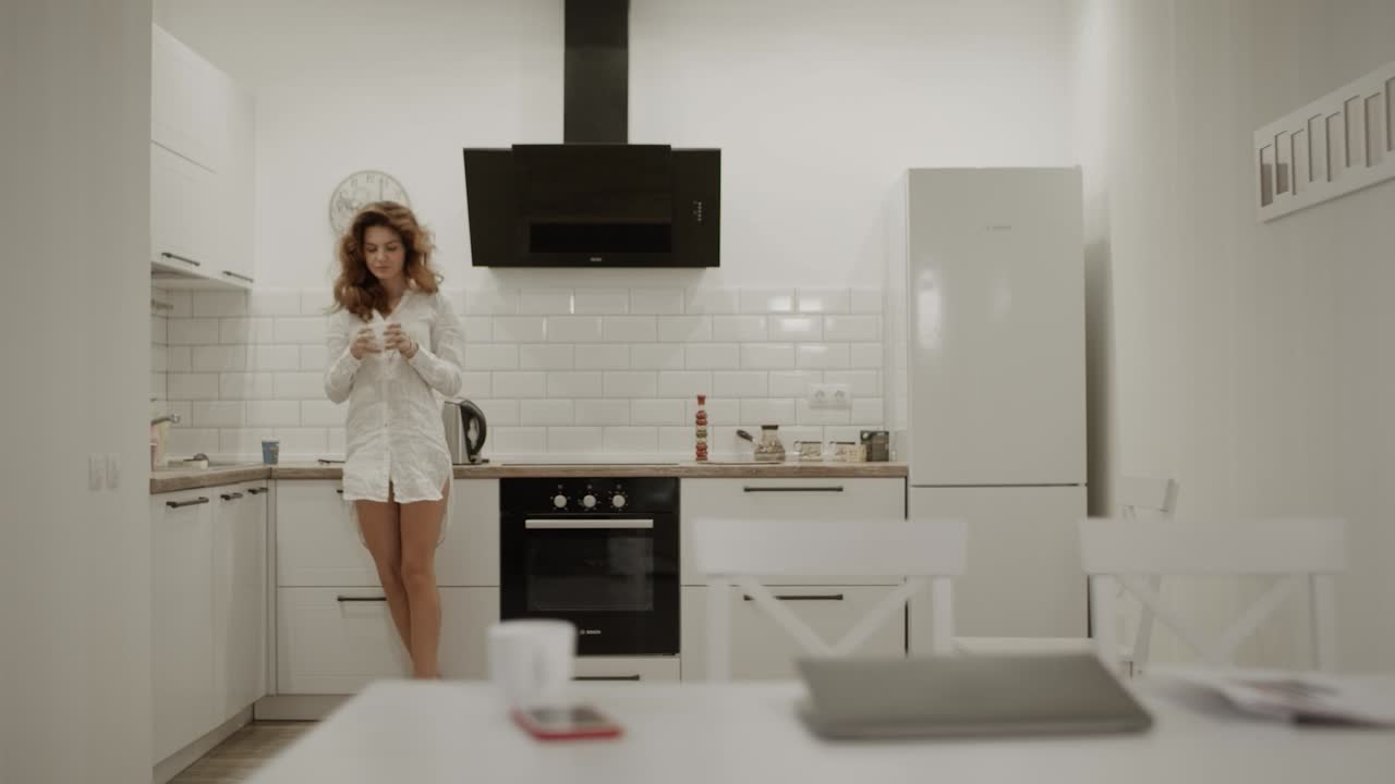 Mutfakta kahve yapan mutlu genç kadın. Gülümseyen kadın mesaj alıyor.