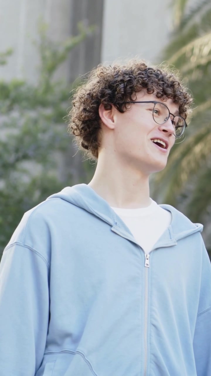 Video verticale: Uomo con felpa blu e occhiali che parla vicino a un muro del cortile, reagendo a un segnale fuori campo.