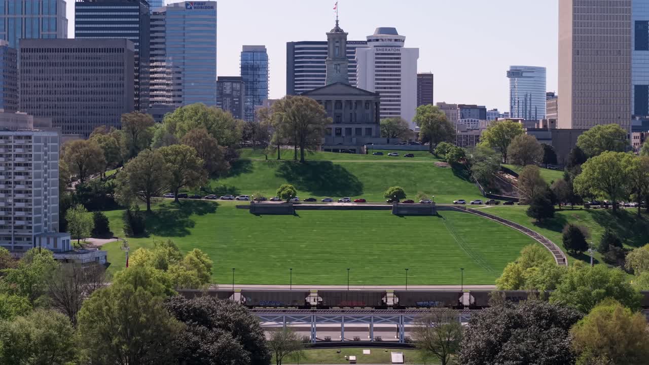 Aerial pull back of State Capitol Building and surrounding office buildings as train goes through in Nashville, Tennessee