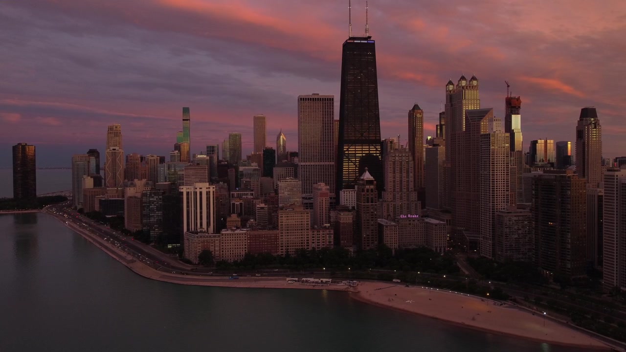 Vid drone-luftfoto av Chicagos skyline ved solnedgang, som fremhever 875 North Michigan Avenue (John Hancock Center), Oak Street Beach og Lake Shore Drive under en levende skumringskveld