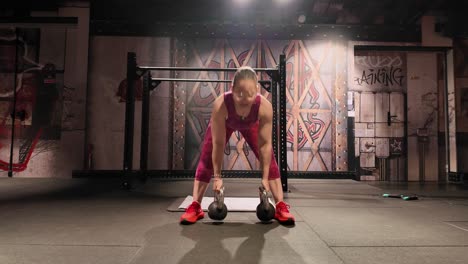 front view of a strong woman exercising in a gym, performing bent-over rows with two kettlebells to build back and arm muscle. strength and conditioning workout