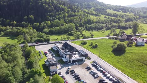 Flight-above-modern-restaurant-with-huge-parking,-green-fields,-forest-and-straight-long-road