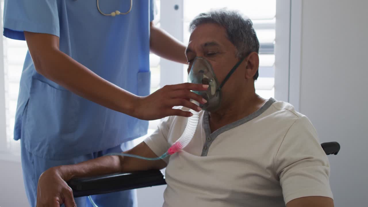 Dottoressa multietnica che assiste un uomo anziano a casa che usa un ventilatore