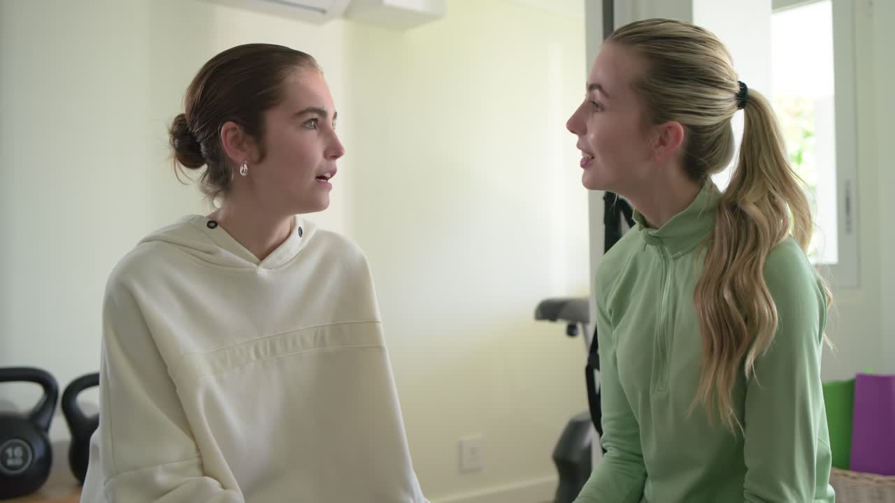 Two female friends scrolling smartphone and laughing, discussing concern and reassuring in home gym