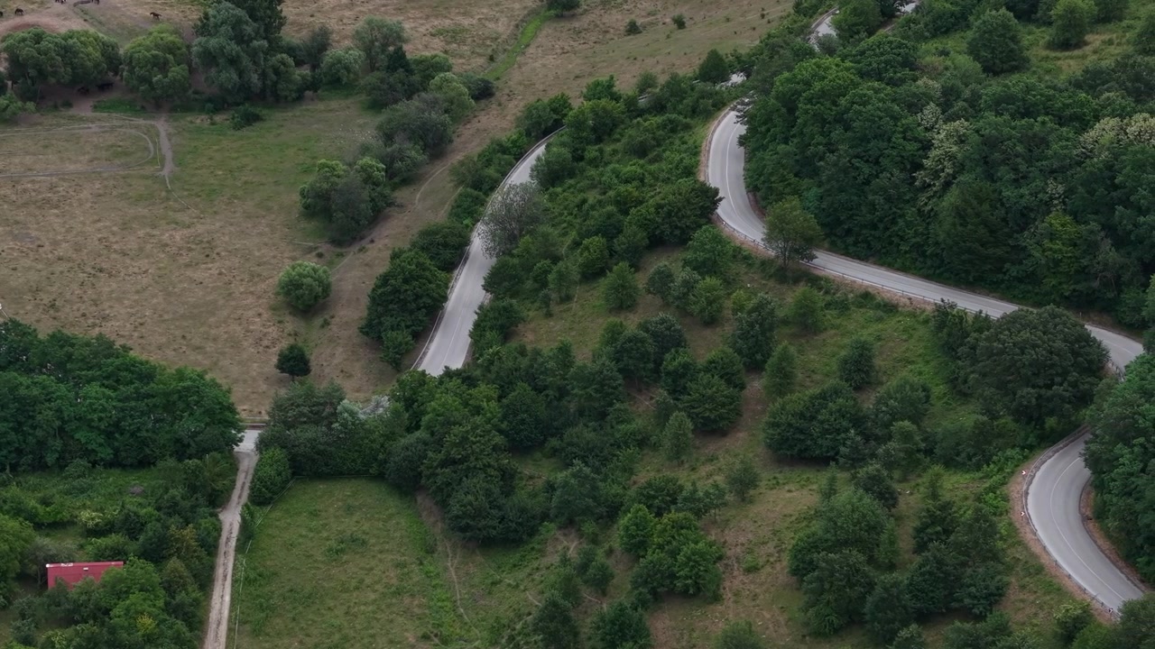 An aerial drone view capturing winding country roads meandering through lush green forests and open rural fields in the countryside.