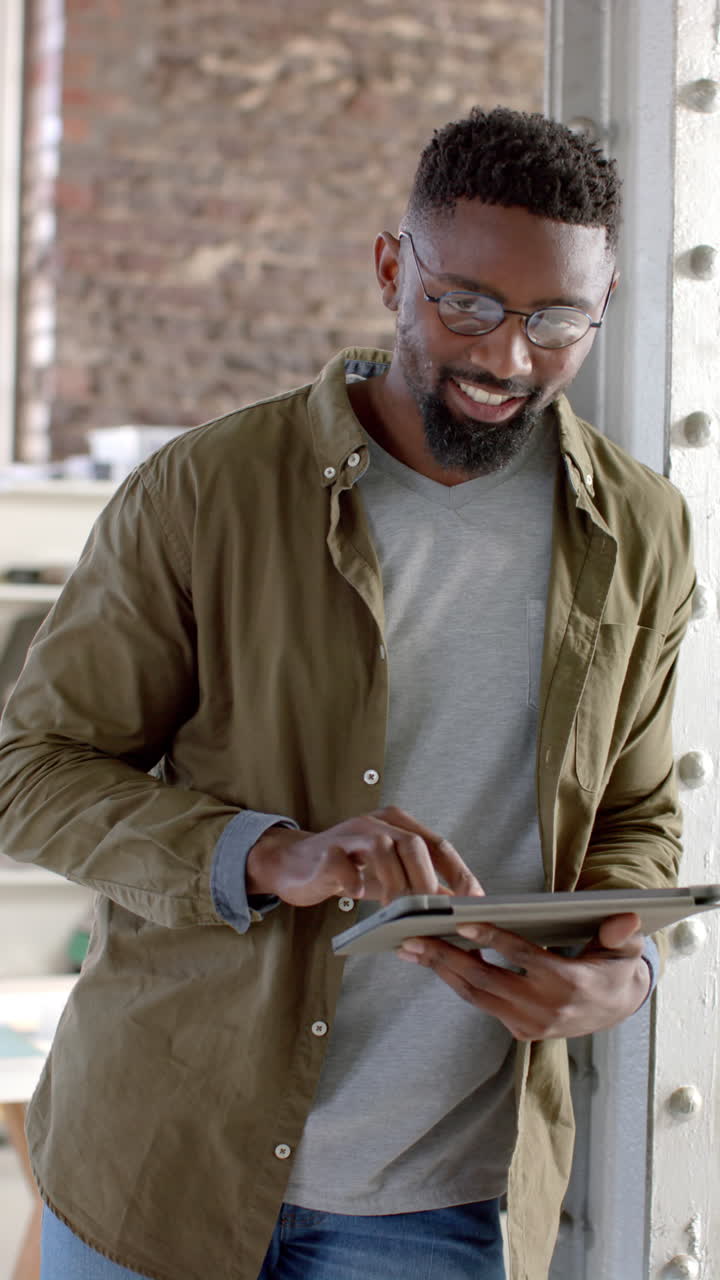 Vertical video of portrait of happy african american casual businessman using tablet in slow motion