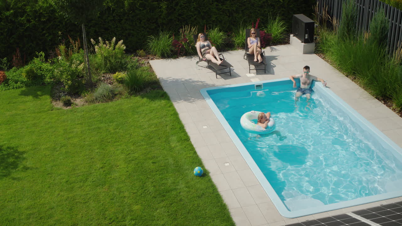 En familie slapper af i poolen, i forgrunden er paneler fra et solcelleanlæg på taget af et sommerhus